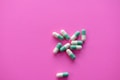 Several green and white capsules are scattered on a vibrant pink background. The capsules are positioned in a loose cluster, displaying their bold colors against the contrasting surface.