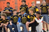 A group of young athletes wearing blue and yellow jerseys are gathered in a gym with climbing walls in the background. The jerseys have numbers and the words 'West Hernando' on them. Some are standing, while others are kneeling, showing camaraderie and team spirit.