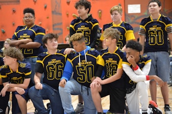 A group of young athletes wearing blue and yellow jerseys are gathered in a gym with climbing walls in the background. The jerseys have numbers and the words 'West Hernando' on them. Some are standing, while others are kneeling, showing camaraderie and team spirit.