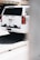 A white police SUV parked on a street, displaying 'Denver Police' on the rear. The word '911 Emergency' is visible along with its license plate. The background shows an urban environment and part of a concrete barrier is also visible.