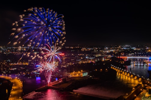 Fireworks bursting in red, white, and blue over the river at night.