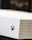 A close-up shot of a gaming console with a white textured surface featuring small circular perforations. The Xbox logo is visible on the side.