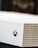A close-up shot of a gaming console with a white textured surface featuring small circular perforations. The Xbox logo is visible on the side.