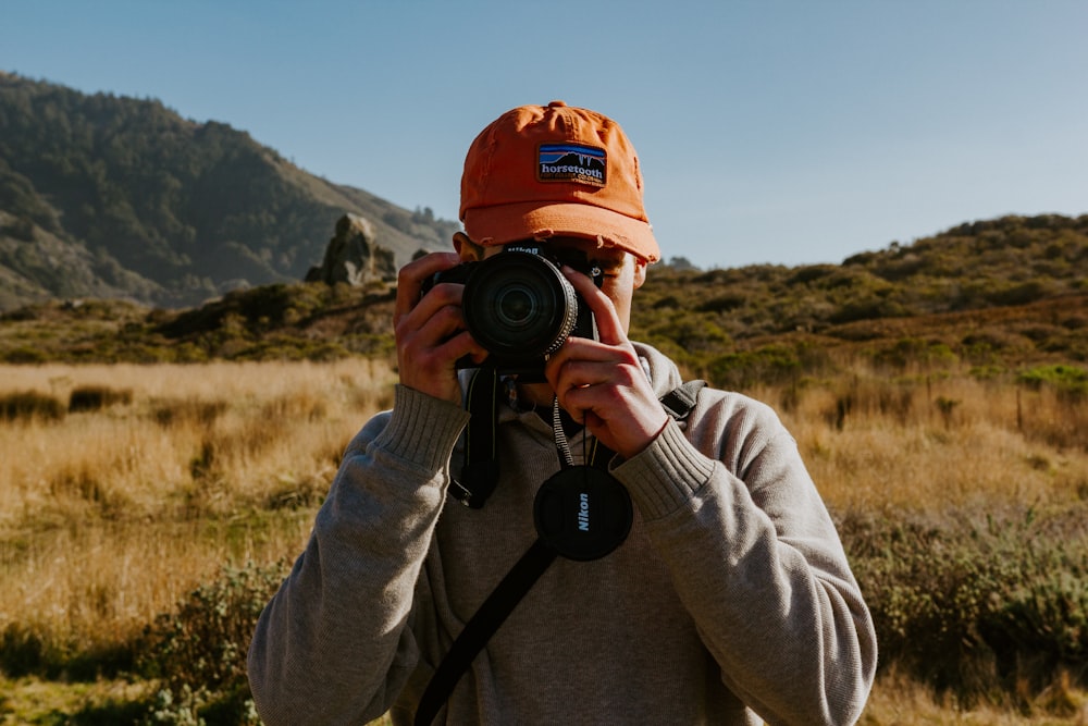 man in brown jacket holding black nikon dslr camera