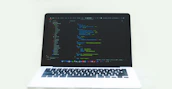 Close-up of hands typing code on a laptop with dark-themed screens and green highlights.