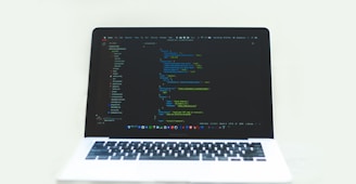 A laptop displaying a code editor with a dark theme, showing lines of colorful code. The environment is bright and minimalistic.