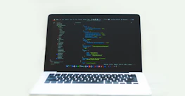 Close-up of hands typing code on a laptop with dark-themed screens and green highlights.