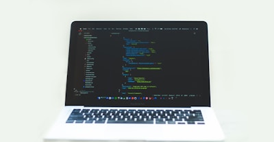 A laptop displaying a code editor with a dark theme, showing lines of colorful code. The environment is bright and minimalistic.