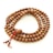 A string of wooden prayer beads arranged in a spiral pattern on a flat surface. Each bead has a smooth, polished texture, and the string is finished with two smaller beads and a red tassel.