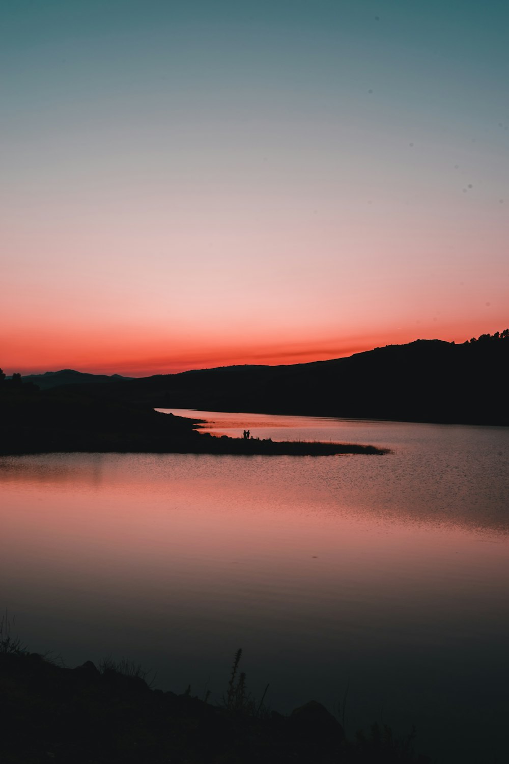 silhouette of mountain near body of water during sunset