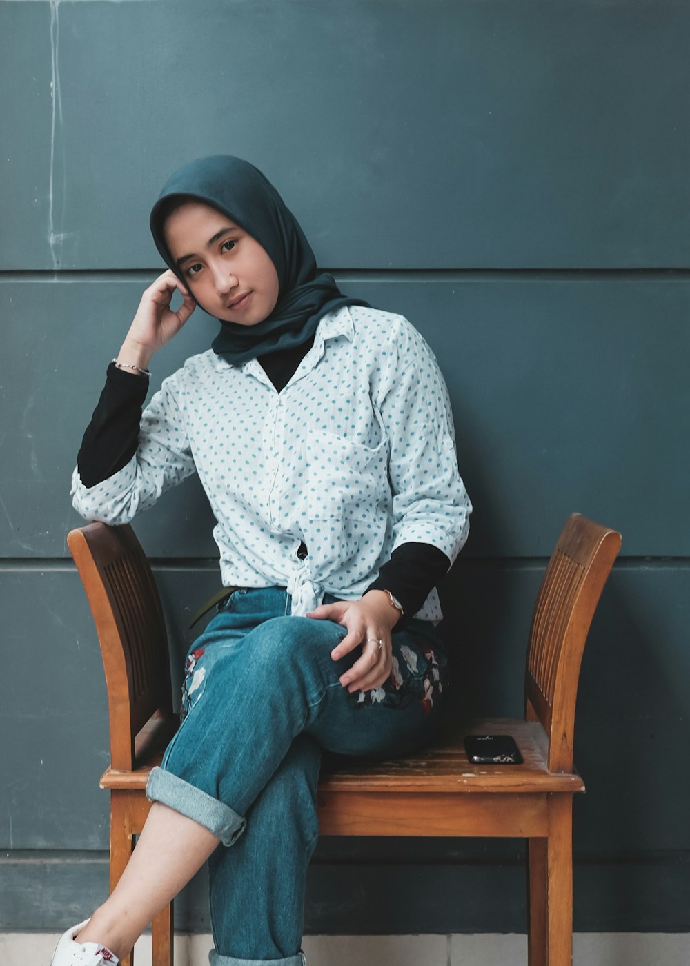 woman in white and black long sleeve shirt and blue denim jeans sitting on brown wooden