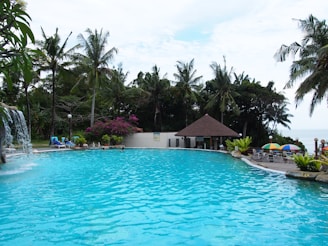 A bright blue pool with crystal-clear water surrounded by lush greenery and a cozy seating area.
