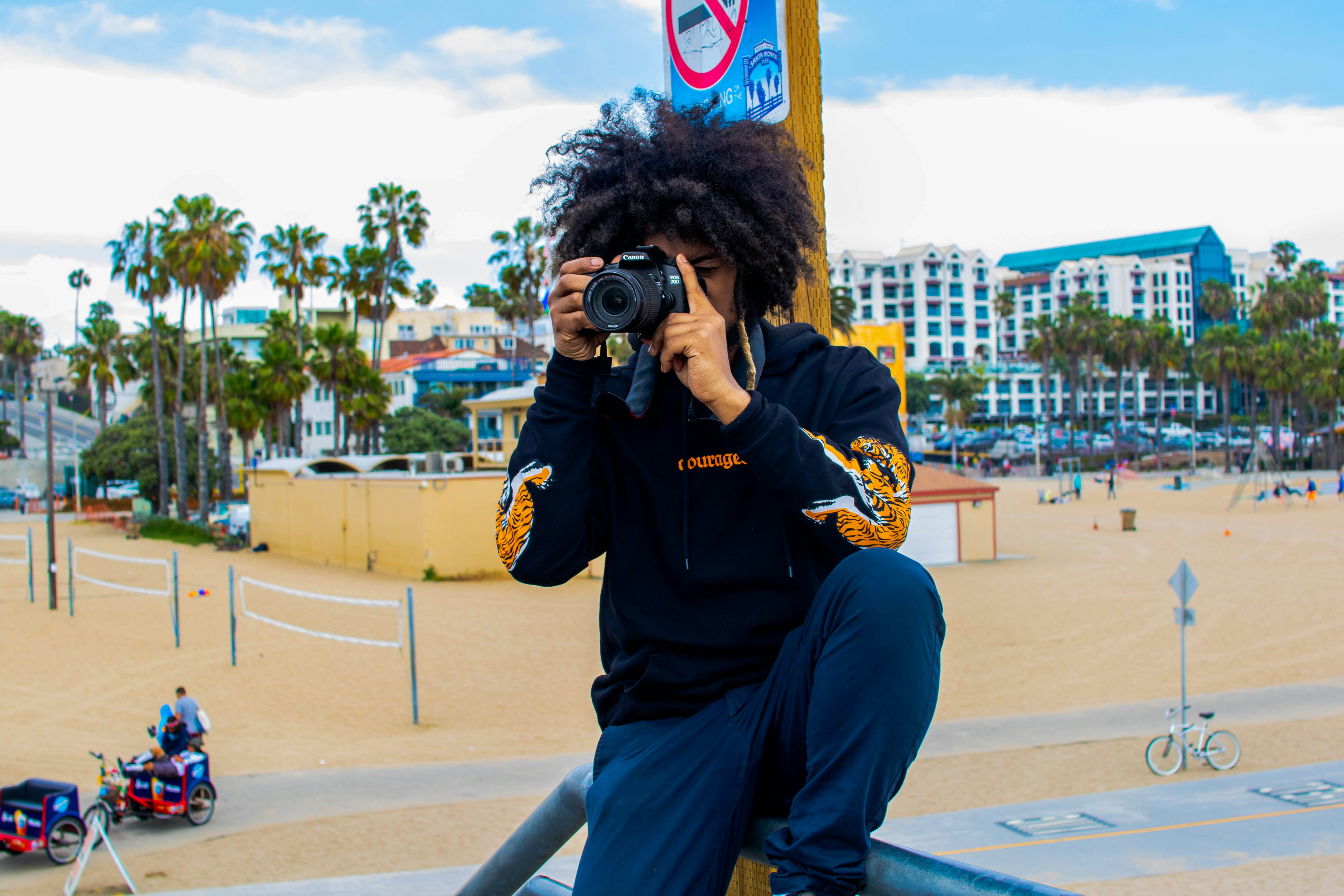 man in black jacket and blue denim jeans sitting on bench using black dslr camera