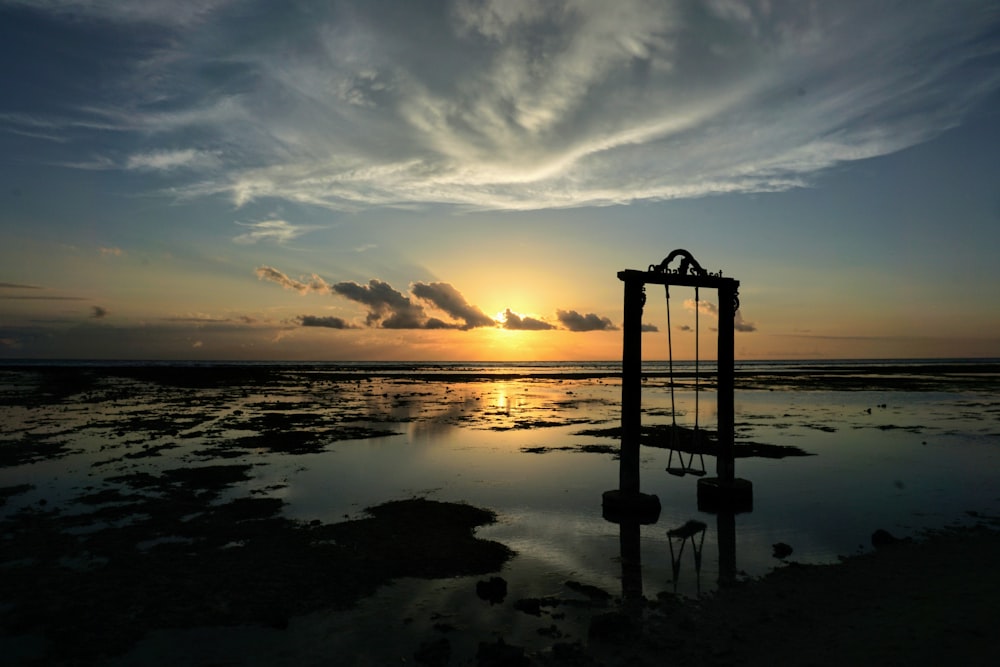 silhouette of person standing on rock formation near body of water during sunset