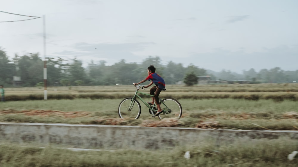 man in red shirt riding bicycle on green grass field during daytime