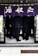 A group of people in suits is seen standing closely together under a traditional Japanese noren curtain with calligraphy. The ground is tiled, and the atmosphere suggests a business meeting or social gathering in a small space.