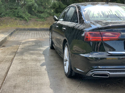 Sleek black car with water droplets beading off after graphene coating treatment.