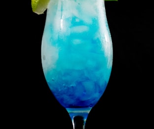 blue liquid in clear drinking glass with sliced lemon