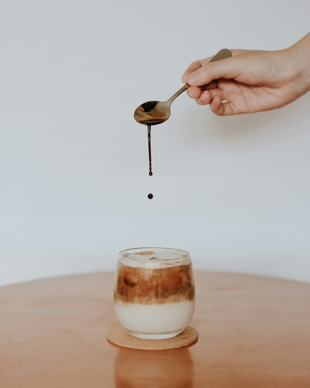 person holding silver spoon and white liquid in clear glass