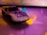 A toy car with a number '931H' printed on its hood, featuring colorful graphics and resting on a surface illuminated by abstract, multi-colored bokeh lights.
