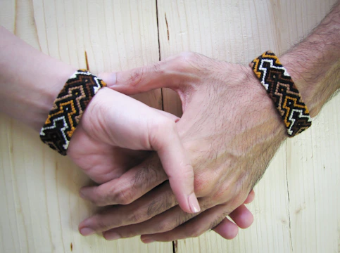 Close-up of intertwined hands with terracotta bracelets, bathed in warm sunlight.