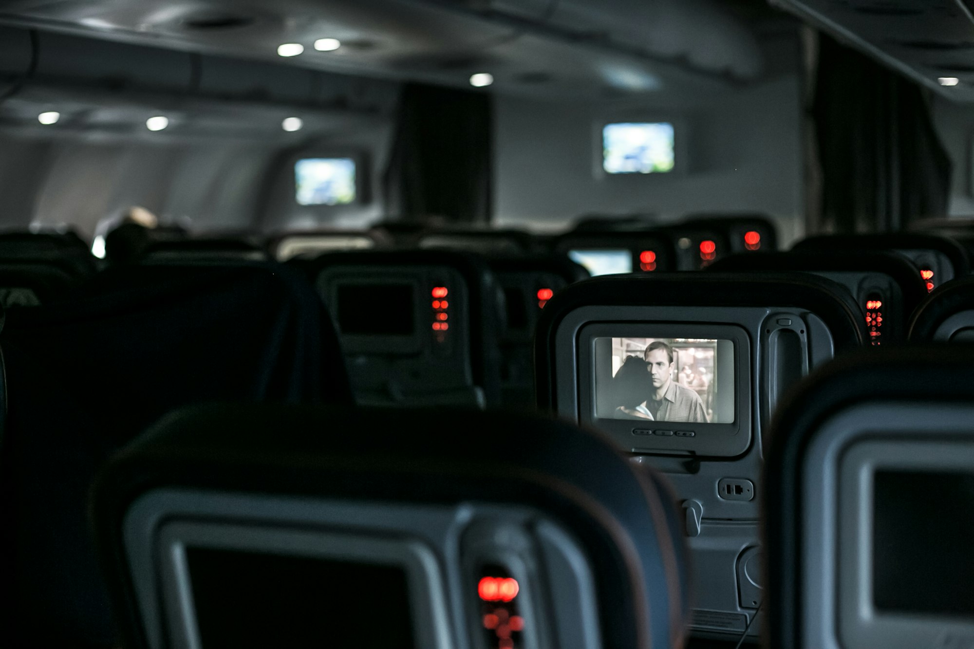 A plane's interior, with empty seats and a movie on a screen.