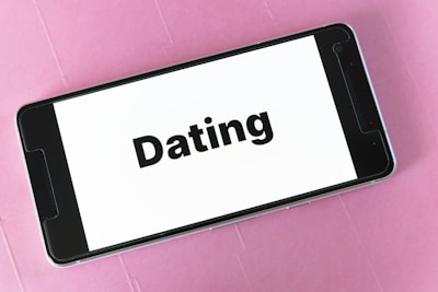 A smartphone displaying the word 'Dating' on its screen, placed on a textured pink surface.
