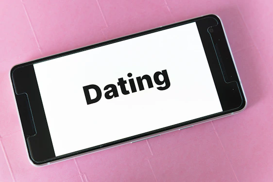 A smartphone displaying the word 'Dating' on its screen, placed on a textured pink surface.