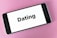 A smartphone displaying the word 'Dating' on its screen, placed on a textured pink surface.
