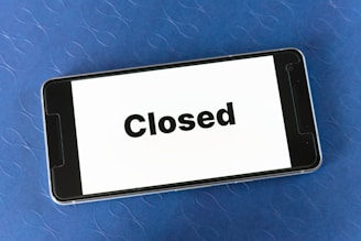 A smartphone displaying the word 'Closed' on its screen is resting on a textured blue surface.