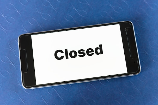 A smartphone displaying the word 'Closed' on its screen is resting on a textured blue surface.