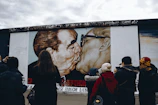 A group of artists and attendees engaging in lively discussion beside a striking queer art mural.