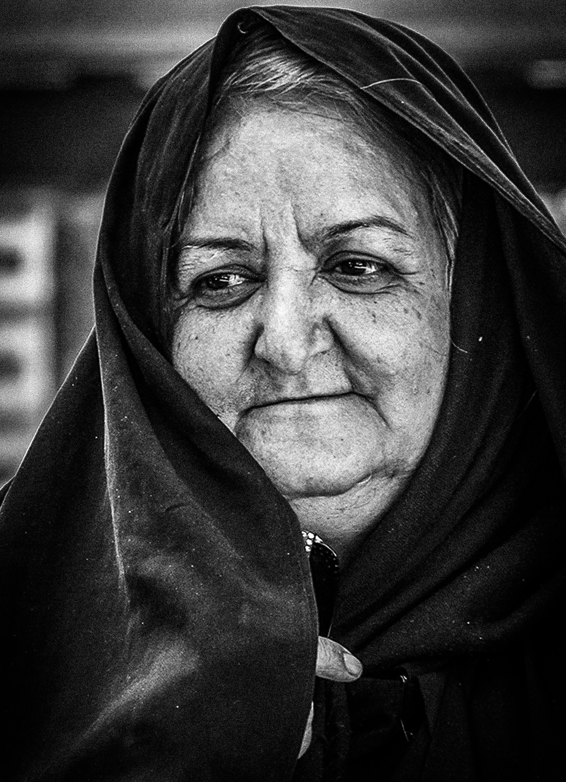 A black and white portrait of an elderly woman with weathered hands, her eyes telling a hundred untold stories.