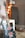 A black electric guitar with unique bullet hole designs is placed on a white table. The guitar has red pickup covers and a vibrantly patterned fretboard. In the background, there is soft, warm lighting with a string of round, multicolored lights and a speaker. A basket containing items is placed on the floor, contributing to a cozy atmosphere.
