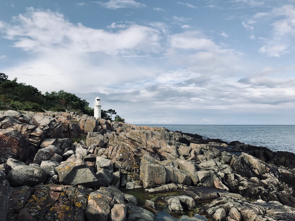 white lighthouse on rocky shore under cloudy sky during daytime