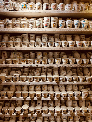 A collection of unique cups with charming designs displayed on a wooden shelf.