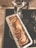 A freshly baked banana bread loaf sits in a rectangular metal pan on a stovetop, next to a silver moka pot. The loaf has slices of banana baked into its top, giving it a rustic appearance.