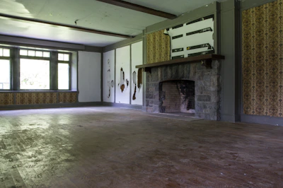 Before photo of a worn-down living room with outdated wallpaper and old carpet.