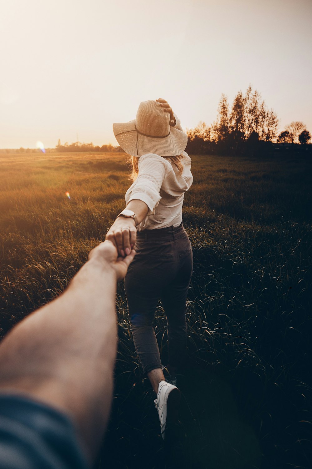 woman in white jacket and blue denim jeans wearing brown sun hat walking on green grass