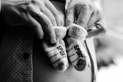 A pair of small striped socks with the word 'SPORT' on them are gently held in someone's hands. The focus is on the socks, which appear soft and cozy. The background is blurred, adding emphasis to the socks and hands.
