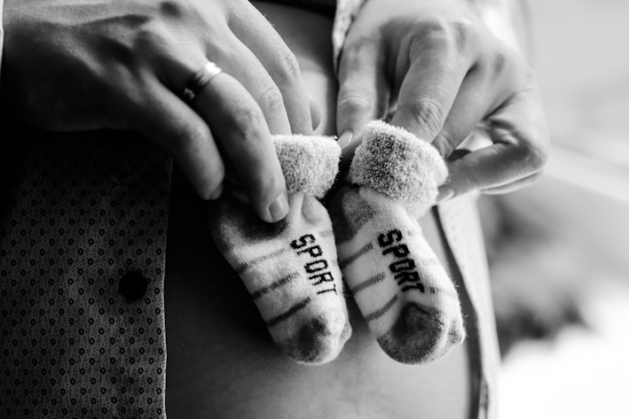 A pair of small striped socks with the word 'SPORT' on them are gently held in someone's hands. The focus is on the socks, which appear soft and cozy. The background is blurred, adding emphasis to the socks and hands.