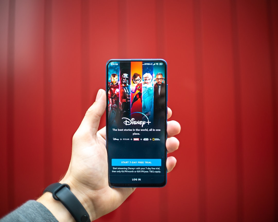 person holding black iphone 4, Disney+ on a Android Phone.
