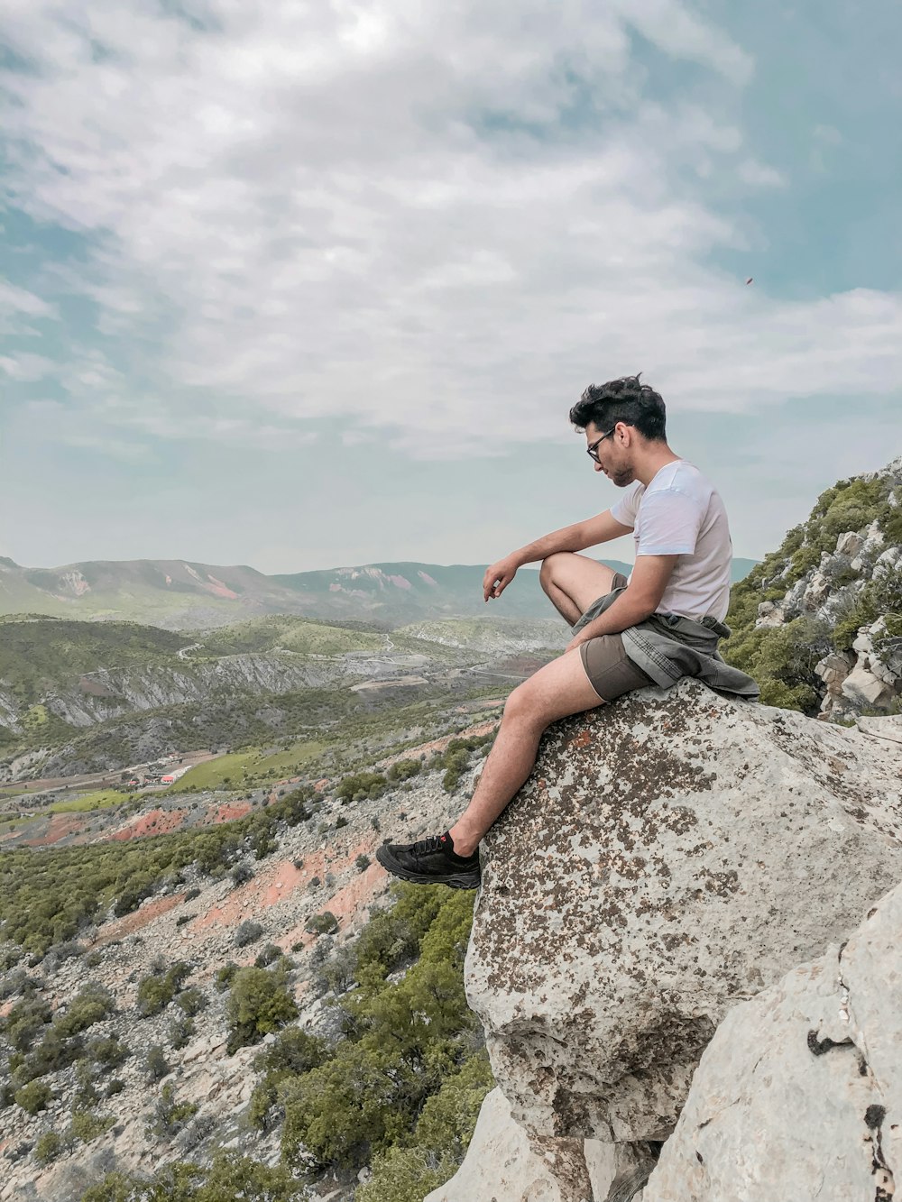 man in white t-shirt sitting on rock during daytime