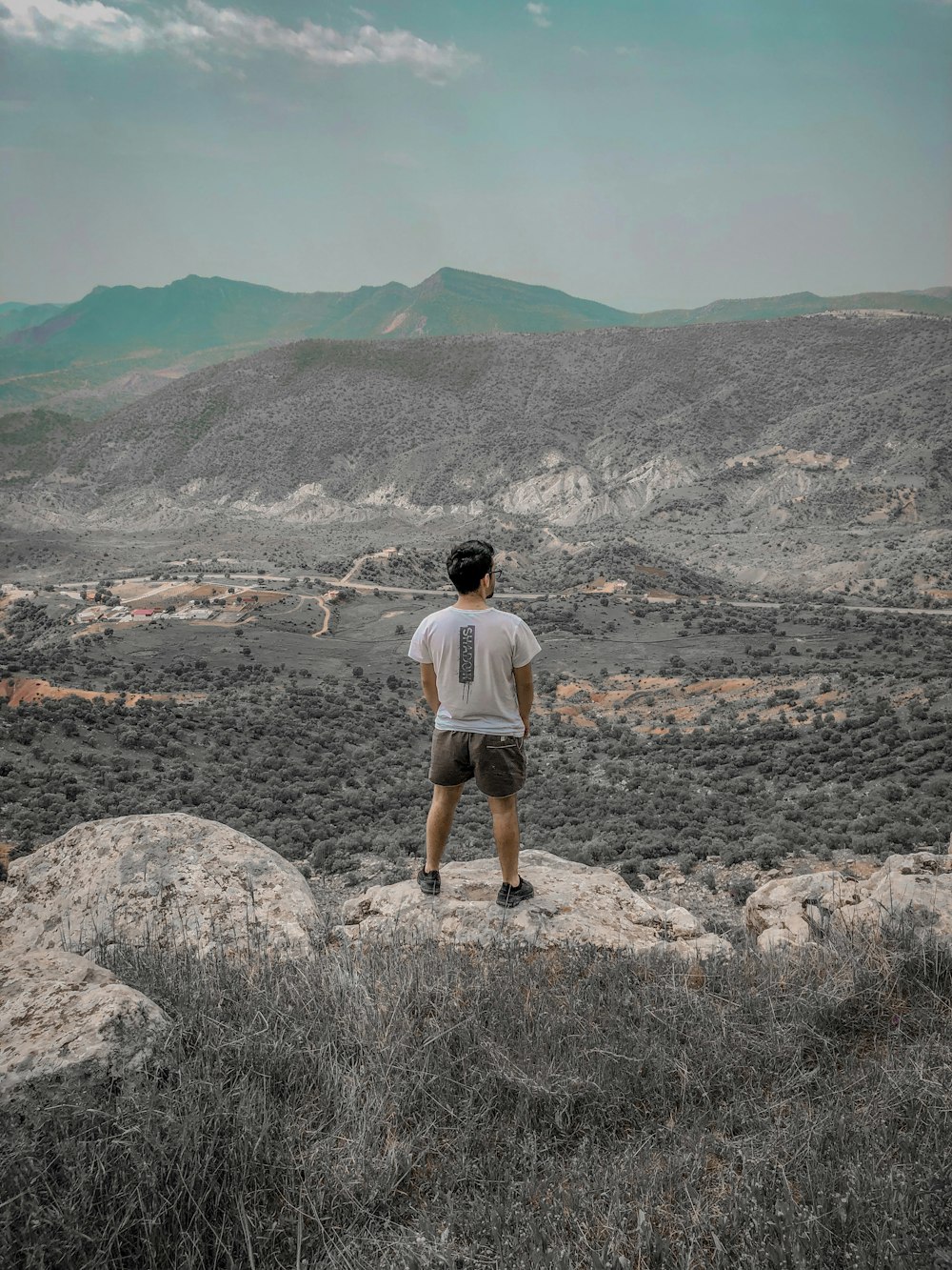 man in white t-shirt and brown shorts standing on rocky ground during daytime