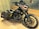 A custom motorcycle with a dark, metallic design featuring shark teeth artwork on the fairing. The bike has a military theme with star insignias and yellow stripes on the side bags. It also boasts large black wheels and a sleek black exhaust system.