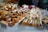 An assortment of pastries and cakes is displayed on platters, featuring a variety of treats topped with fresh berries, icing, and cream. The arrangement includes cupcakes, loaf cakes, and tarts, with labels indicating different flavors.