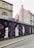 A series of artistic murals painted on a wall, featuring stylized profiles of faces in monochrome, interspersed with vibrant red petals. The wall is set along a street with older buildings in the background, showcasing a blend of architectural and artistic elements.