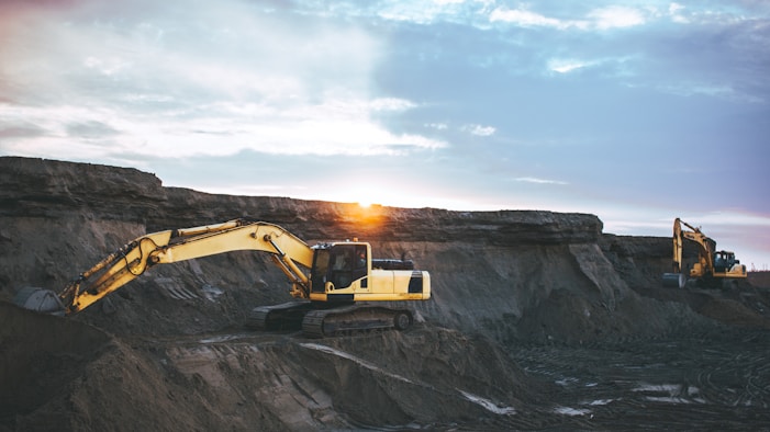 A rugged mining site at sunrise with workers collaborating near heavy machinery.