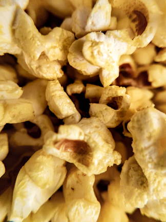 A close-up view of freshly popped popcorn with a texture that showcases the fluffy, irregular shapes and the golden-yellow hue of the kernels. The detailed image highlights the intricate patterns and crispy surfaces, conveying a sense of freshness and appeal.