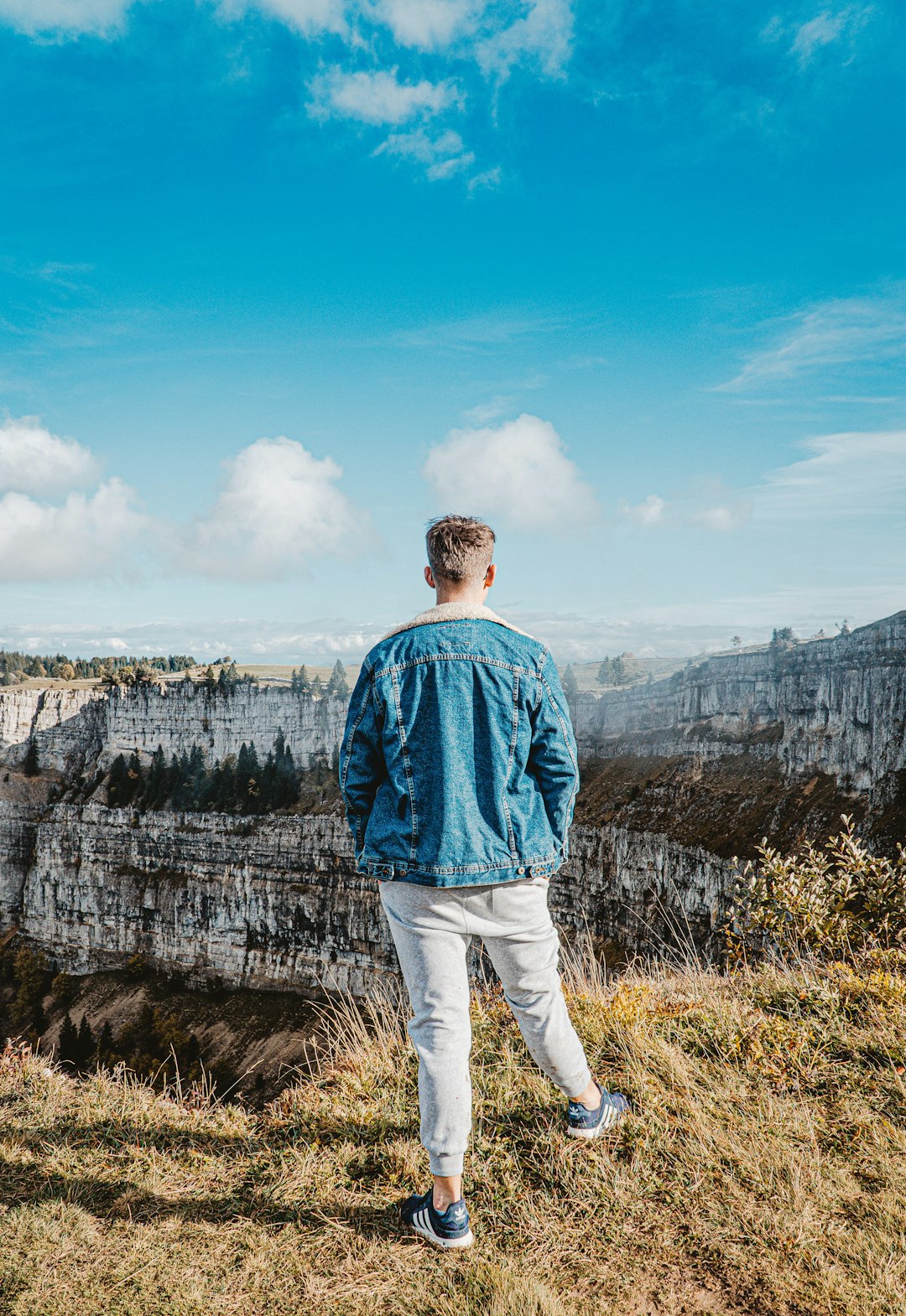 man in blue dress shirt standing on cliff during daytime